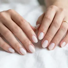 Dłonie z subtelnymi paznokciami delikatnymi, w kolorze mlecznej bieli. Złota bransoletka i pierścionek dodają elegancji.