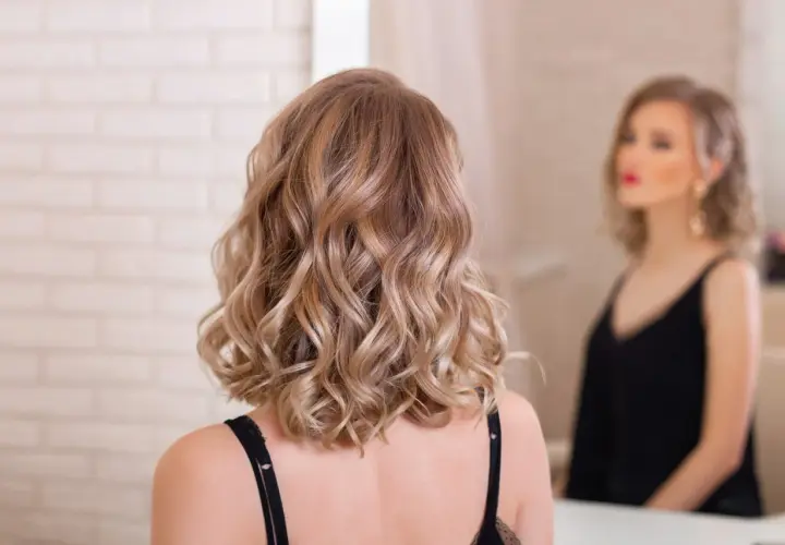 Kobieta z falowanymi blond włosami, idealne wygodne fryzury dla mamy, by wyglądać stylowo i czuć się swobodnie.
