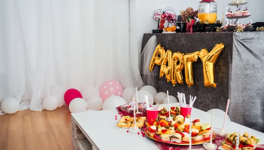 Urocze pomysły na wieczór panieński w domu: złote balony z napisem "PARTY", przekąski i różowe akcenty.