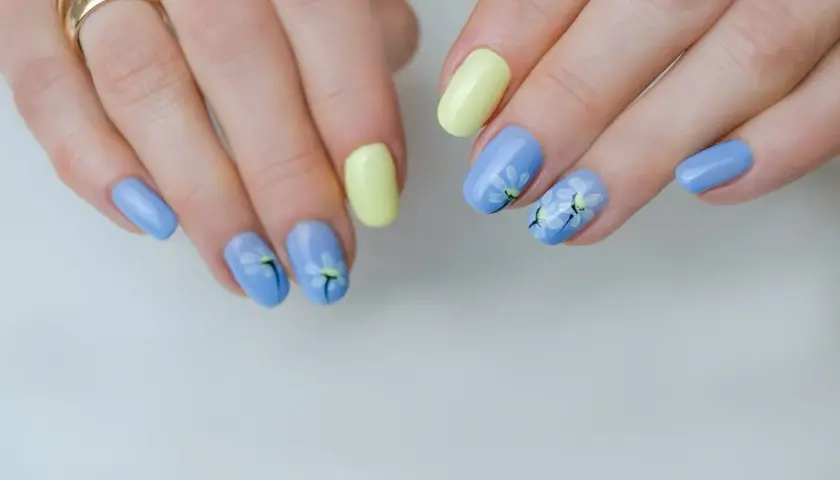 Delikatne kwiaty na paznokciach w pastelowych kolorach: błękitnym i żółtym. Wiosenny manicure z motywem stokrotek.