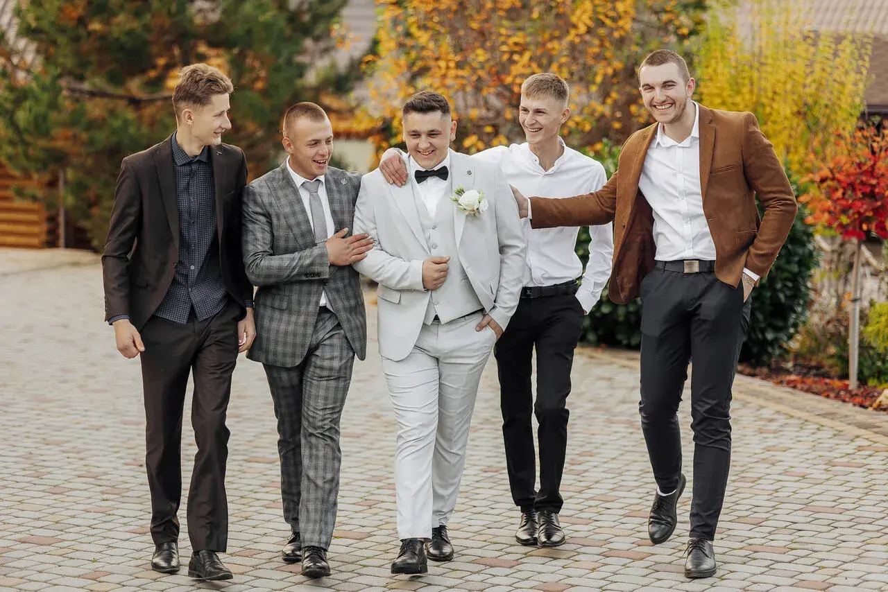 Pięciu mężczyzn w eleganckich garniturach idzie razem. Inspiracja, jak ubrać się na wesele mężczyzna.