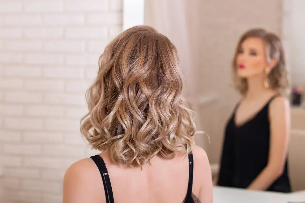 Kobieta z falowanymi blond włosami, idealne wygodne fryzury dla mamy, by wyglądać stylowo i czuć się swobodnie.