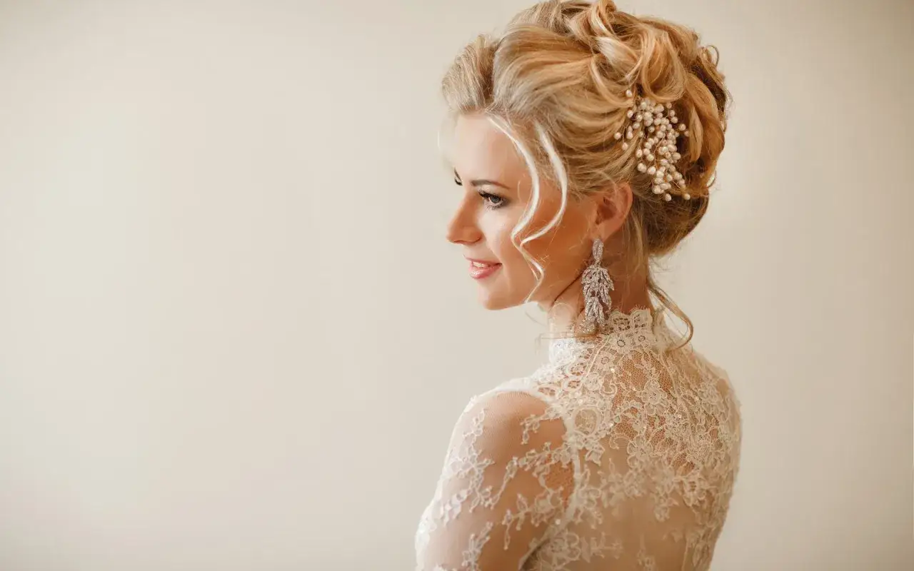 Elegancka fryzura do długiej sukienki na wesele, ozdobiona perłami i kryształowymi kolczykami.