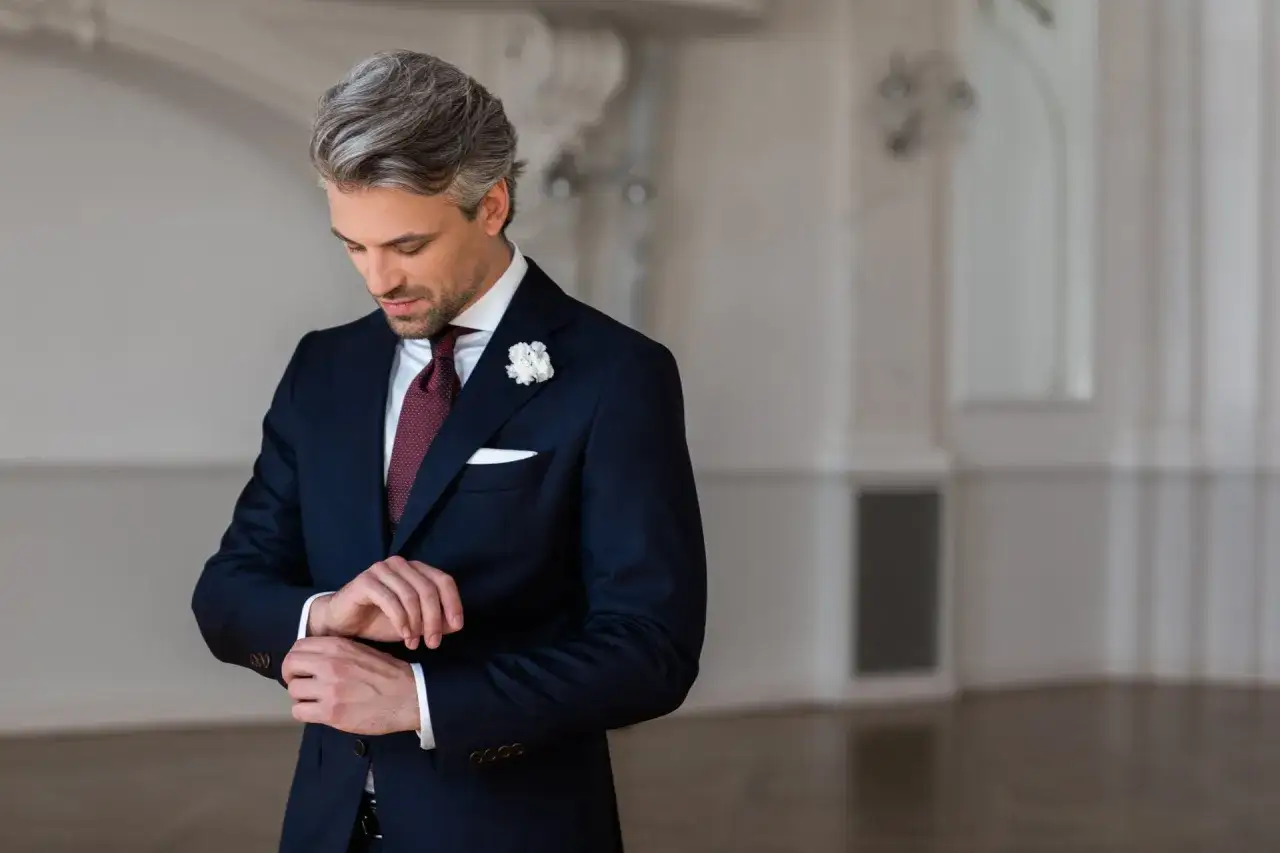 Elegancki mężczyzna poprawia mankiet koszuli, dopasowując ją do granatowej marynarki i bordowego krawata.